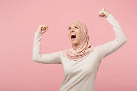 Happy young arabian muslim woman in hijab light clothes posing isolated on pink background. People...