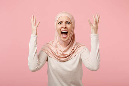 Shocked irritated arabian muslim woman in hijab light clothes posing isolated on pink background. People religious Islam lifestyle concept. Mock up copy space. Screaming, swearing, spreading hands.の写真素材