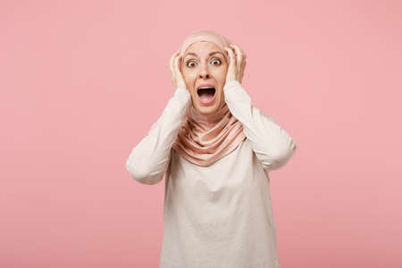 Shocked scared young arabian muslim woman in hijab light clothes posing isolated on pink background....