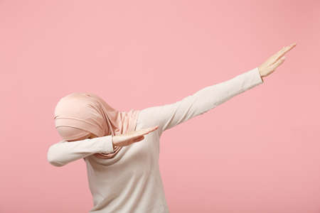 Young arabian muslim woman in hijab light clothes posing isolated on pink wall background studio...