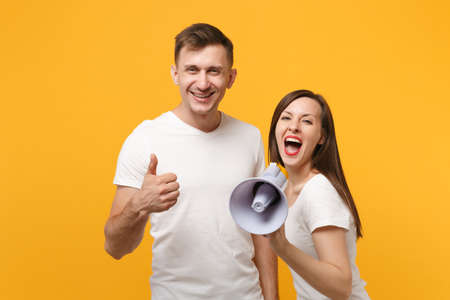 Cheerful young couple friends guy girl in white blank empty t-shirts posing isolated on yellow...