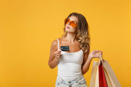 Pensive young woman girl in eyeglasses posing isolated on yellow orange background. People lifestyle concept. Mock up copy space. Holding package bag with purchases after shopping, credit bank card.の写真素材