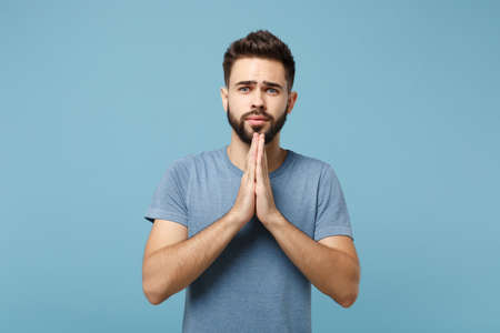 Young serious handsome man in casual clothes posing isolated on blue wall background, studio...