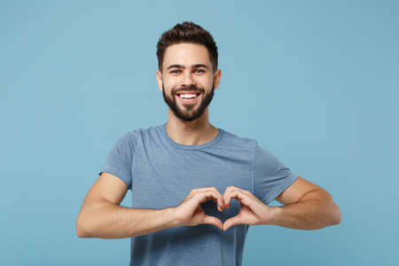 Young smiling handsome man in casual clothes posing isolated on blue wall background, studio portrait. People lifestyle concept. Mock up copy space. Showing shape heart with hands, heart-shape sign.の写真素材