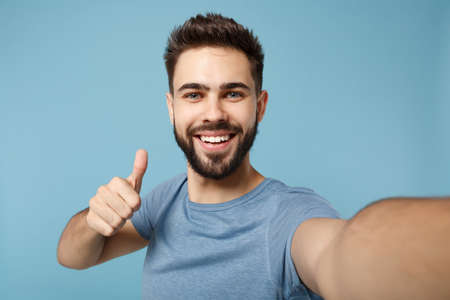 Close up Young handsome man in casual clothes posing isolated on blue background studio portrait. People lifestyle concept. Mock up copy space. Doing selfie shot on mobile phone, showing thumb up.の写真素材