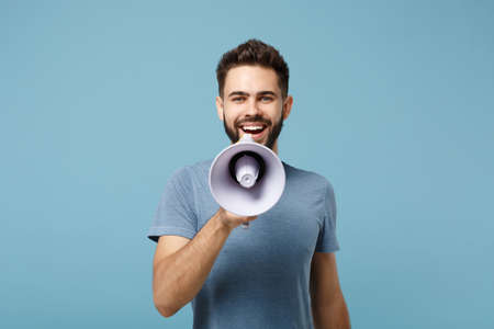 Young smiling attractive man in casual clothes posing isolated on blue wall background, studio portrait. People sincere emotions lifestyle concept. Mock up copy space. Holding, Scream in megaphone.の写真素材