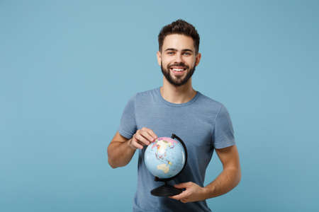 Young smiling handsome man in casual clothes posing isolated on blue wall background, studio portrait. People sincere emotions lifestyle concept. Mock up copy space. Holding in hands world globe.の写真素材