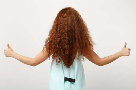 Back rear view of young redhead woman girl in casual light clothes posing isolated on white background studio portrait. People lifestyle concept. Mock up copy space. Spreading hands showing thumbs up.の写真素材
