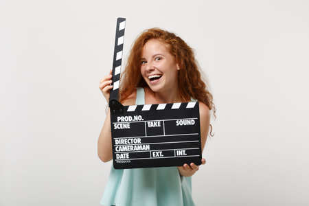 Young funny redhead woman girl in casual light clothes posing isolated on white wall background in studio. People lifestyle concept. Mock up copy space. Holding classic black film making clapperboard.の写真素材