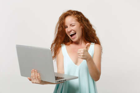 Young funny redhead woman girl in casual light clothes posing isolated on white wall background. People lifestyle concept. Mock up copy space. Working on laptop pc computer showing thumb up, blinking.の写真素材
