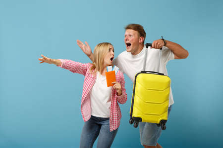 Couple friends guy girl in white pink t-shirts posing isolated on pastel blue background. People lifestyle concept. Mock up copy space. Hold passport boarding pass, ticket, suitcase, running and late.の写真素材
