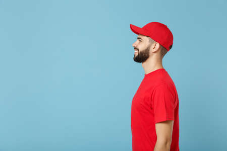 Delivery man in red uniform workwear isolated on blue wall background, studio portrait. Professional...