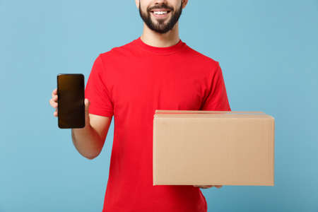 Delivery man in red uniform isolated on blue background, studio portrait. Male employee in cap...