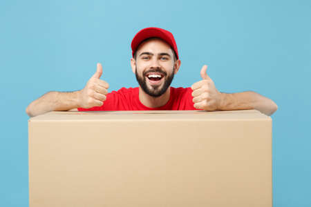 Delivery man in red uniform isolated on blue background, studio portrait. Male employee in cap...