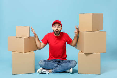 Delivery man in red uniform isolated on blue background, studio portrait. Male employee in cap...