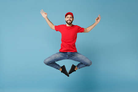 Delivery man in red uniform workwear isolated on blue wall background, studio portrait. Professional male employee in cap t-shirt print working as courier dealer. Service concept. Mock up copy space.の写真素材