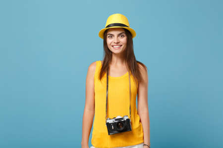 Traveler tourist woman in yellow summer casual clothes, hat with photo camera isolated on blue background. Female passenger traveling abroad to travel on weekends getaway. Air flight journey concept.の写真素材