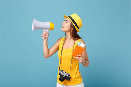 Traveler tourist woman in yellow casual clothes hat hold tickets megaphone camera isolated on blue background. Female passenger traveling abroad travel on weekends getaway. Air flight journey concept.の写真素材