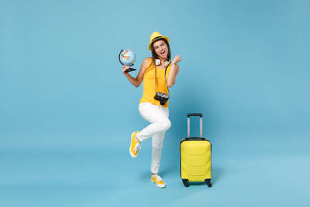 Traveler tourist woman in yellow casual clothes, hat with suitcase photo camera isolated on blue background. Female passenger traveling abroad to travel on weekends getaway. Air flight journey conceptの写真素材