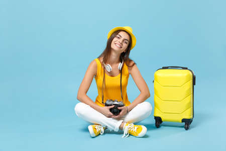 Traveler tourist woman in yellow casual clothes, hat with suitcase photo camera isolated on blue background. Female passenger traveling abroad to travel on weekends getaway. Air flight journey conceptの写真素材