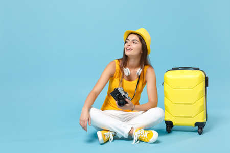 Traveler tourist woman in yellow casual clothes, hat with suitcase photo camera isolated on blue background. Female passenger traveling abroad to travel on weekends getaway. Air flight journey conceptの写真素材