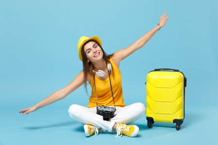 Traveler tourist woman in yellow casual clothes, hat with suitcase photo camera isolated on blue background. Female passenger traveling abroad to travel on weekends getaway. Air flight journey conceptの写真素材