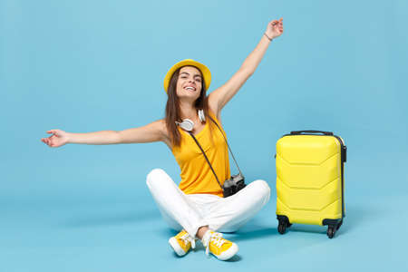 Traveler tourist woman in yellow casual clothes, hat with suitcase photo camera isolated on blue background. Female passenger traveling abroad to travel on weekends getaway. Air flight journey conceptの写真素材