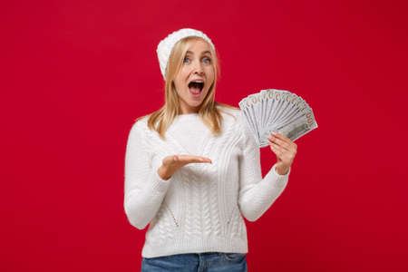 Excited young woman in white sweater, hat isolated on red wall background. Healthy fashion...