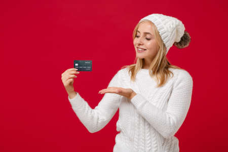 Smiling pretty young woman in white sweater, hat isolated on red wall background studio portrait....