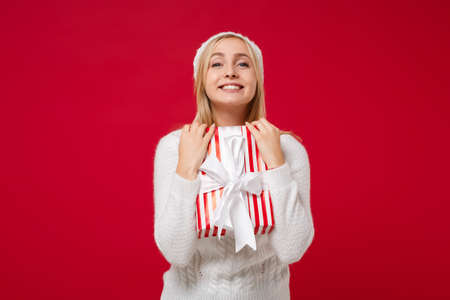 Joyful young woman in white sweater, hat isolated on red wall background. New Year 2020, Valentines...