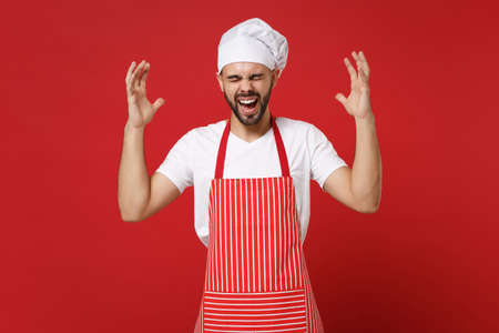 Screaming bearded male chef cook or baker man in striped apron t-shirt toque chefs hat posing isolated on red background. Cooking food concept. Mock up copy space. Keeping eyes closed spreading hands.の写真素材