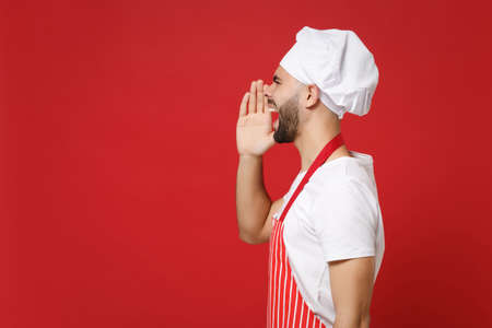 Side view of bearded male chef cook or baker man in striped apron toque chefs hat posing isolated on red background. Cooking food concept. Mock up copy space. Screaming with hand gesture near mouth.の写真素材
