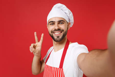 Close up of chef cook baker man in striped apron toque chefs hat posing isolated on red background....