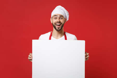 Excited young male chef cook or baker man in toque chefs hat isolated on red background. Cooking food concept. Mock up copy space. Holding big white empty blank billboard with place for text or image.の写真素材
