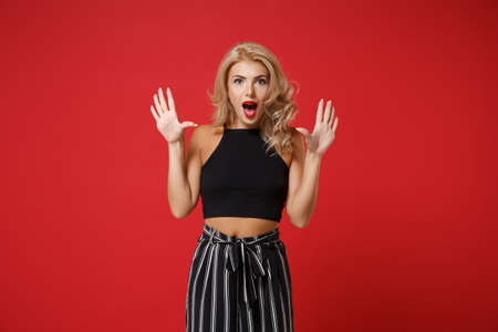 Excited young woman girl in black casual clothes posing isolated on red wall background studio portrait. People sincere emotions lifestyle concept. Mock up copy space. Keeping mouth open rising hands.の写真素材