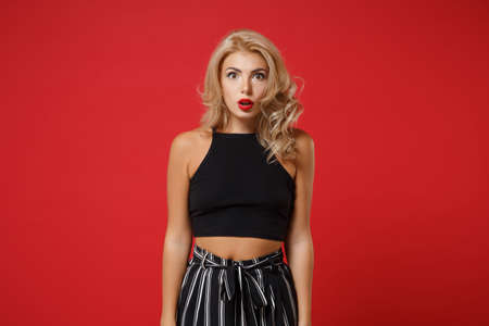 Shocked amazed young woman girl in black casual clothes posing isolated on bright red wall background studio portrait. People sincere emotions lifestyle concept. Mock up copy space. Looking camera.の写真素材