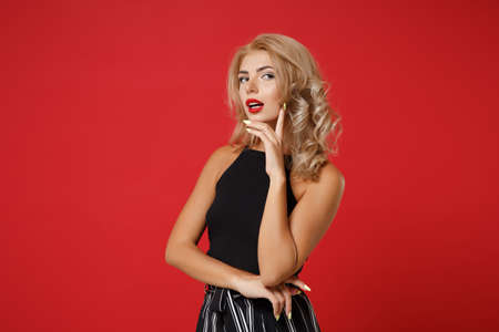 Pensive young woman girl in black clothes posing isolated on red wall background studio portrait. People sincere emotions lifestyle concept. Mock up copy space. Put hand prop up on chin looking aside.の写真素材