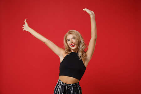 Laughing cheerful funny young woman girl in black clothes posing isolated on bright red wall background studio portrait. People sincere emotions lifestyle concept. Mock up copy space. Rising hands.の写真素材