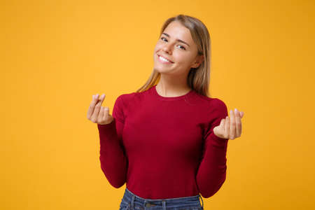 Smiling young blonde woman girl in casual clothes posing isolated on yellow orange wall background. People lifestyle concept. Mock up copy space. Rubbing fingers showing cash gesture asking for money.の写真素材