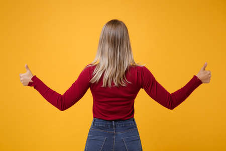 Back rear view of young blonde woman girl in casual clothes posing isolated on yellow orange wall background studio portrait. People emotions lifestyle concept. Mock up copy space. Showing thumbs up.の写真素材