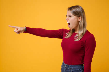 Side view of nervous young blonde woman girl in casual clothes posing isolated on yellow orange background in studio. People lifestyle concept. Mock up copy space. Point index finger aside, swearing.の写真素材
