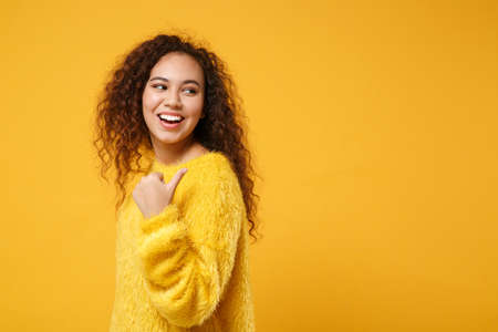 Side view of laughing young african american girl in fur sweater posing isolated on yellow orange...
