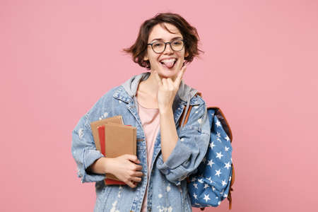 Funny young woman student in denim clothes glasses backpack posing isolated on pastel pink background.の写真素材