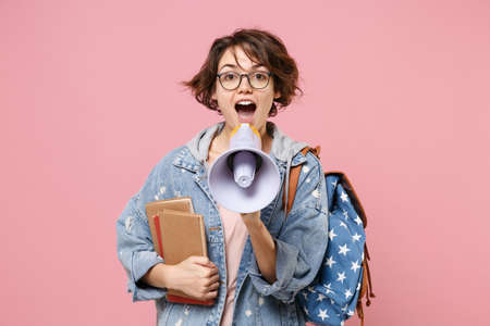 Funny young woman student in denim clothes, eyeglasses, backpack posing isolated on pastel pink...