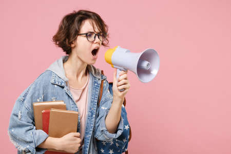 Concerned young woman student in denim clothes, eyeglasses, backpack posing isolated on pastel pink background.の写真素材