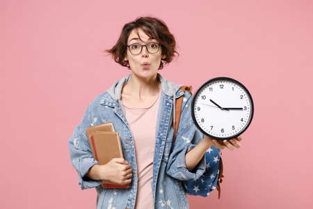 Amazed young woman student in denim clothes eyeglasses, backpack posing isolated on pastel pink background.の写真素材