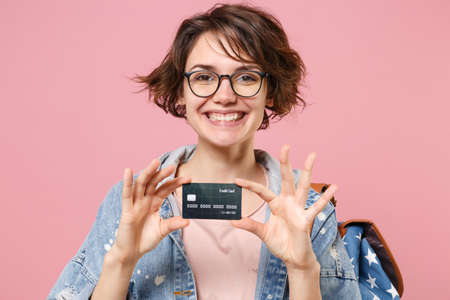 Pretty young woman student in denim clothes glasses backpack posing isolated on pastel pink...