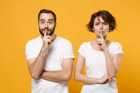 Secret couple friends bearded guy girl in white t-shirts posing isolated on yellow orange background. People lifestyle concept.の写真素材