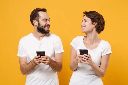 Laughing young couple friends bearded guy girl in white blank empty t-shirts isolated on yellow orange background.の写真素材