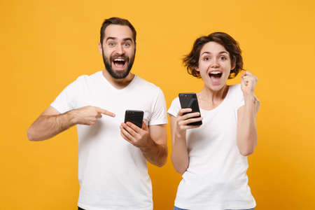 Excited couple friends bearded guy girl in white t-shirts isolated on yellow orange background.の写真素材